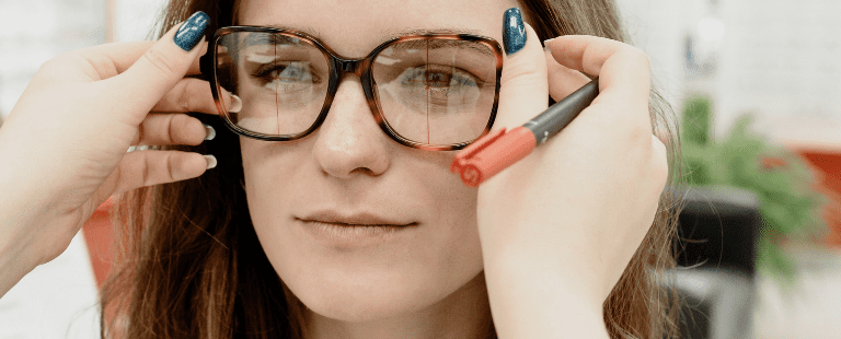 Mulher experimentando óculos com ajuda de outra pessoa.