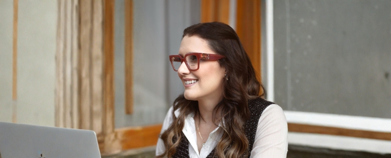 Mulher sorridente usando óculos, trabalhando no computador.