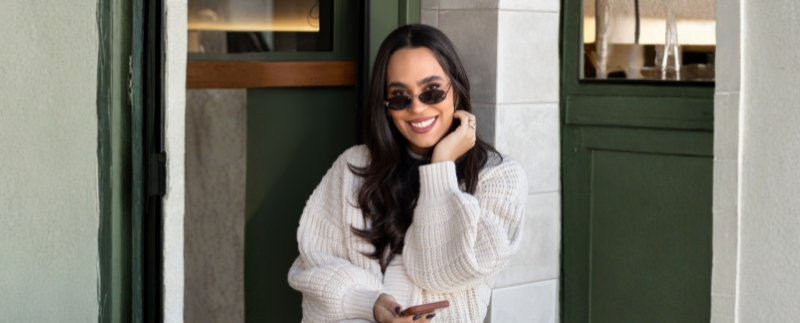 Mulher sorrindo com óculos escuros e suéter branco