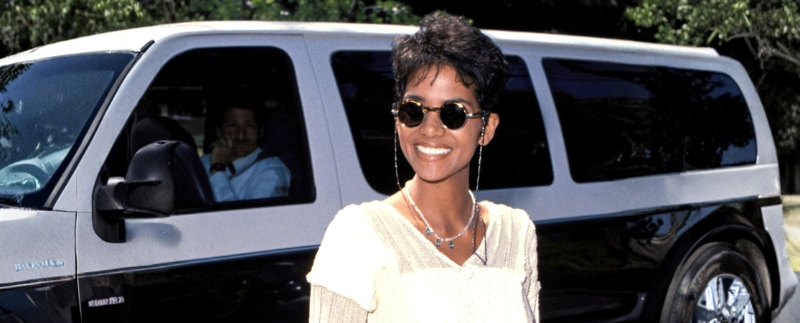 Mulher sorrindo ao lado de um carro elegante.